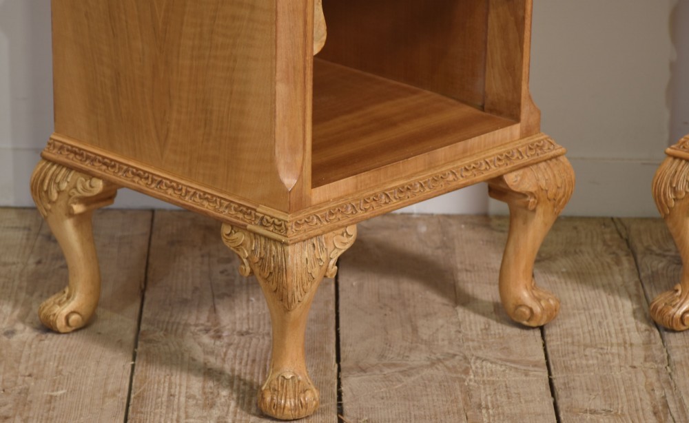 A pair of golden burr walnut bedside cabinets featuring two upper drawers with brass drop handles above an open cubby, set on carved cabriole legs with claw and ball feet. View V