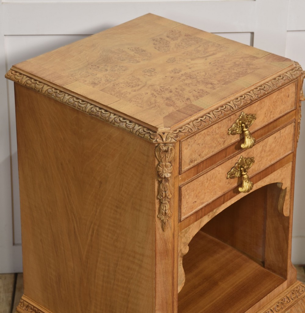 A pair of golden burr walnut bedside cabinets featuring two upper drawers with brass drop handles above an open cubby, set on carved cabriole legs with claw and ball feet. View IX