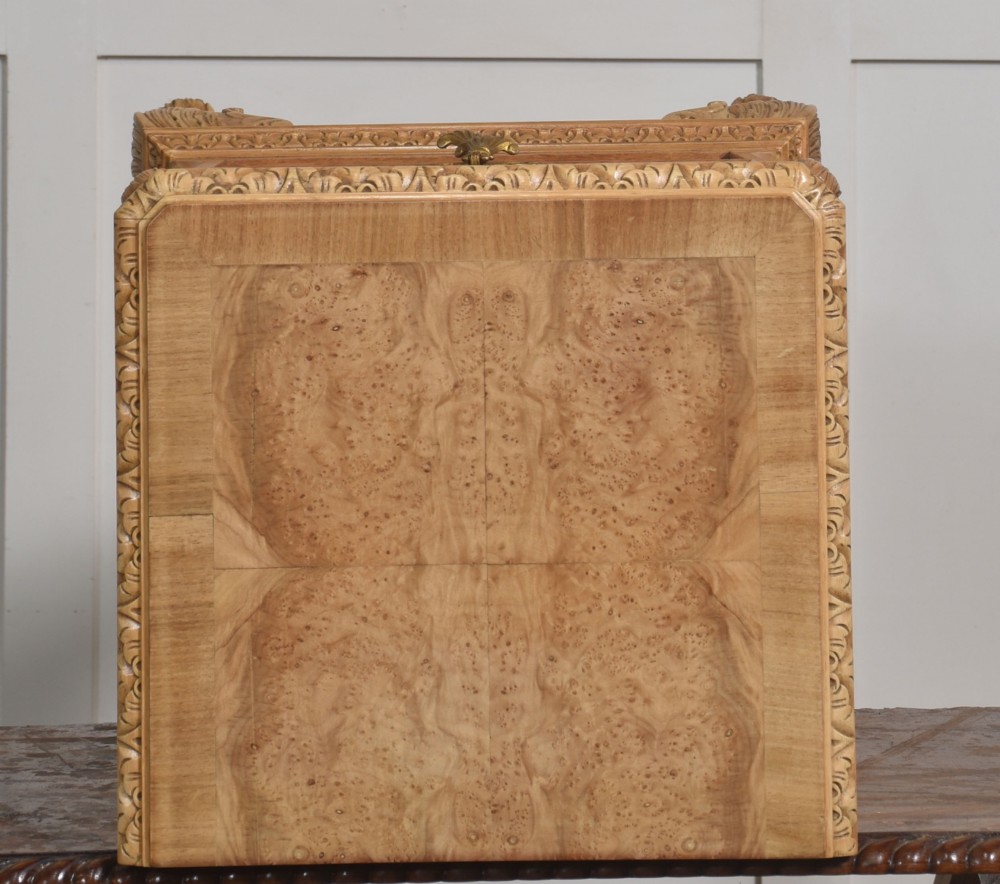 A pair of golden burr walnut bedside cabinets featuring two upper drawers with brass drop handles above an open cubby, set on carved cabriole legs with claw and ball feet. View X