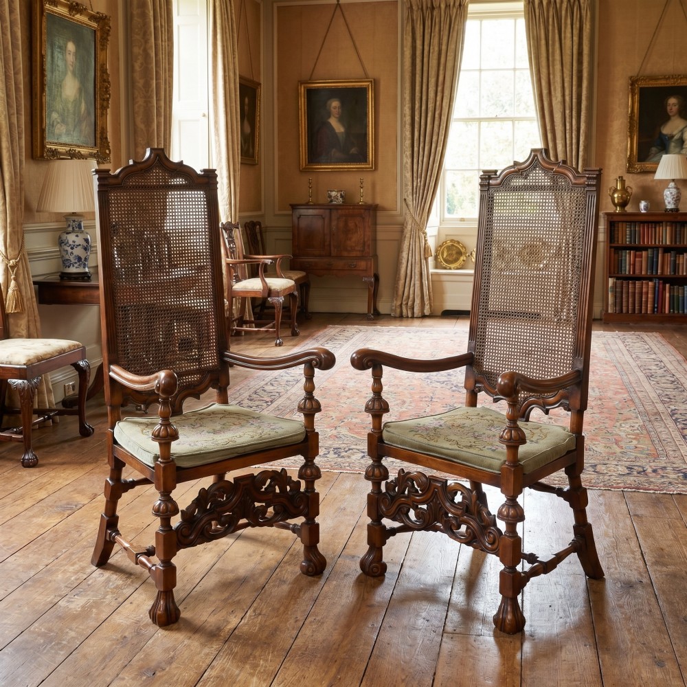 A pair of high-backed carved walnut open armchairs featuring tall cane panels, turned supports, intricate scrolling stretchers, and floral needlepoint cushions. View II