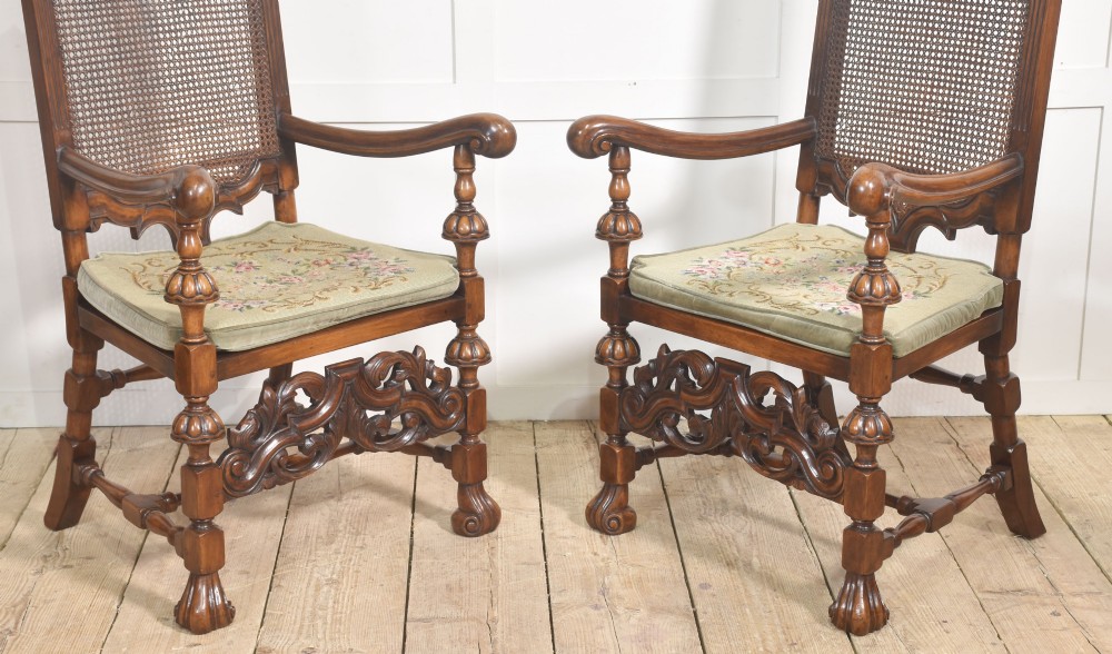 A pair of high-backed carved walnut open armchairs featuring tall cane panels, turned supports, intricate scrolling stretchers, and floral needlepoint cushions. View III