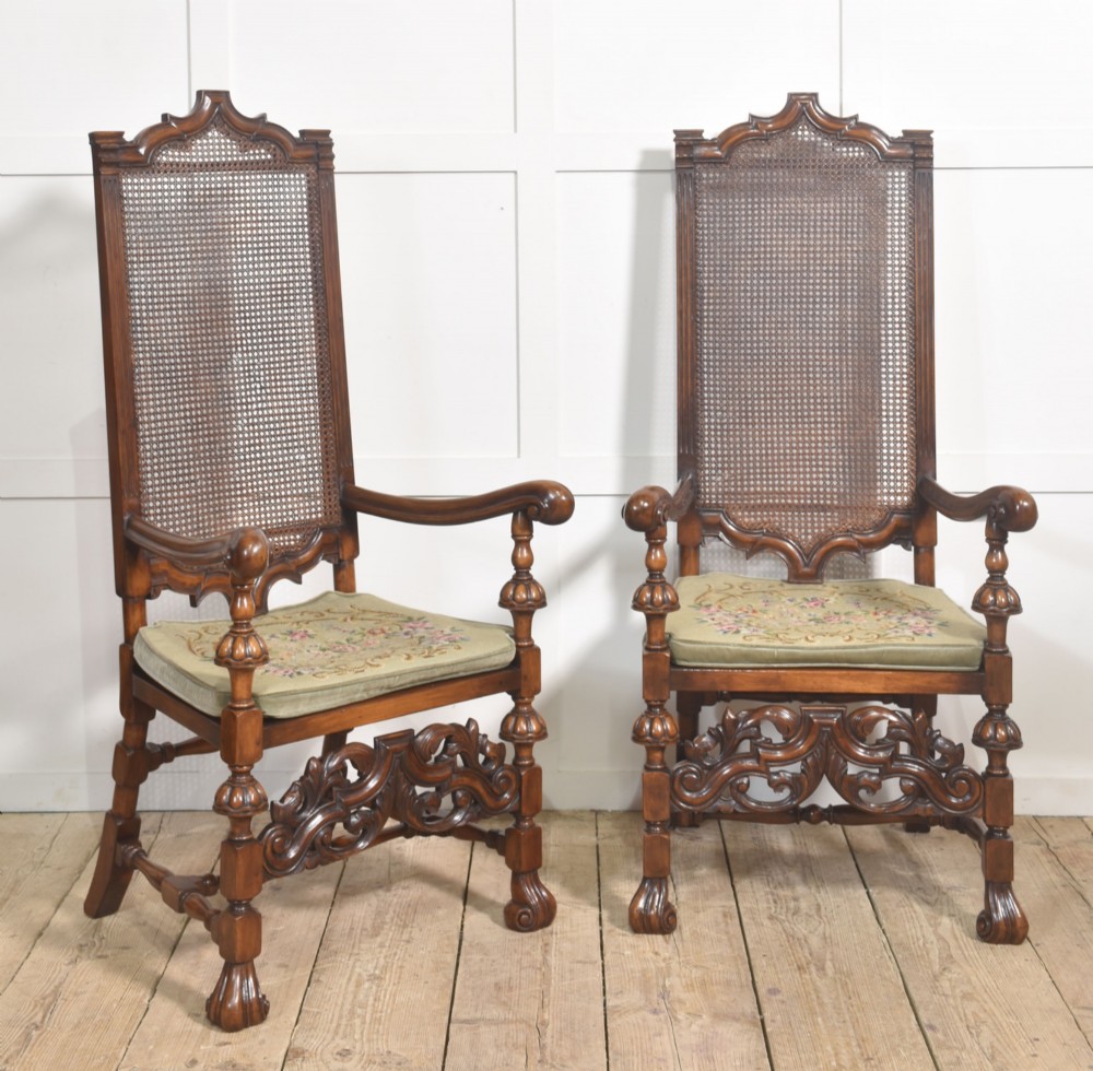 A pair of high-backed carved walnut open armchairs featuring tall cane panels, turned supports, intricate scrolling stretchers, and floral needlepoint cushions. View V