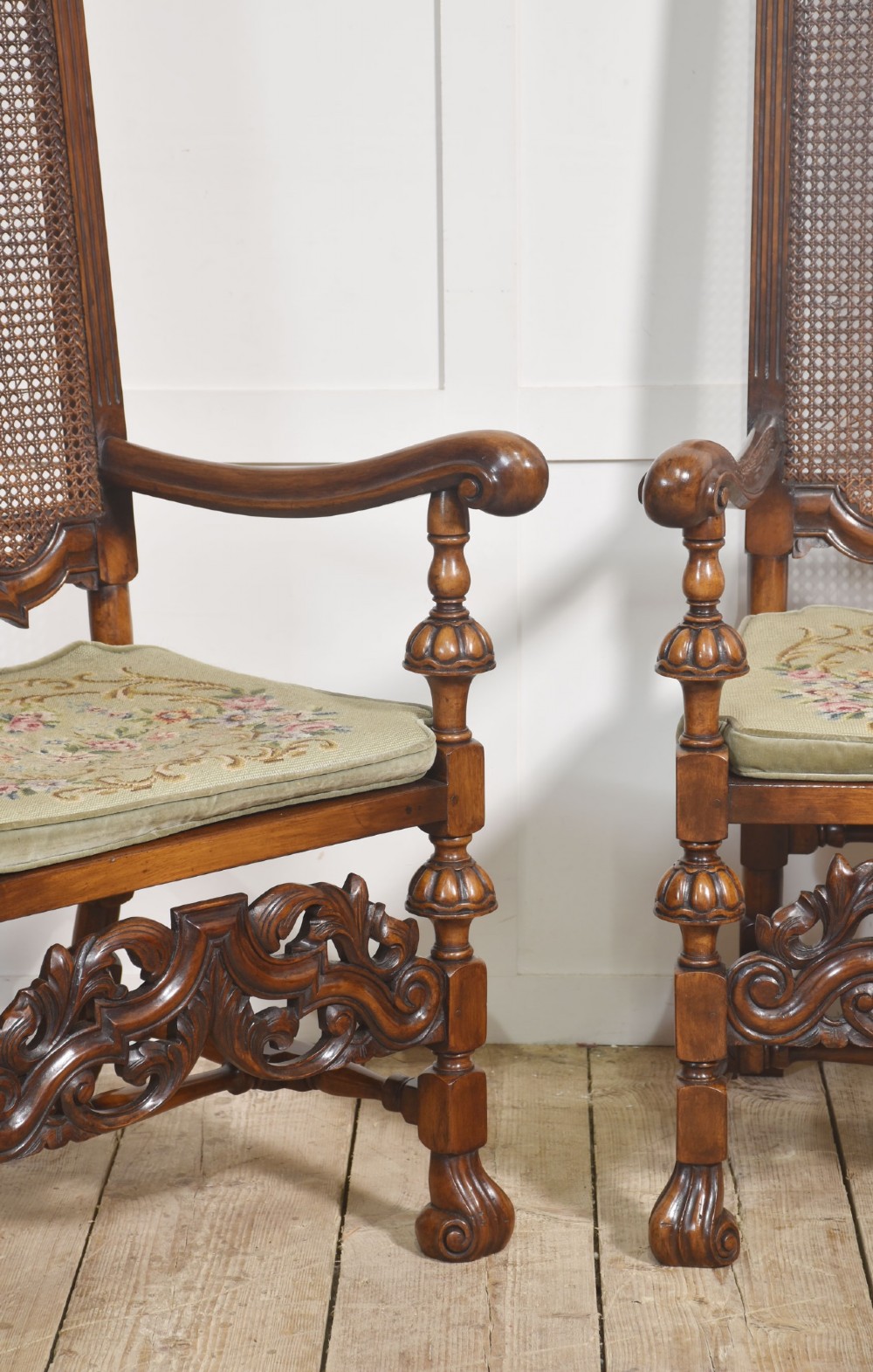 A pair of high-backed carved walnut open armchairs featuring tall cane panels, turned supports, intricate scrolling stretchers, and floral needlepoint cushions. View VI