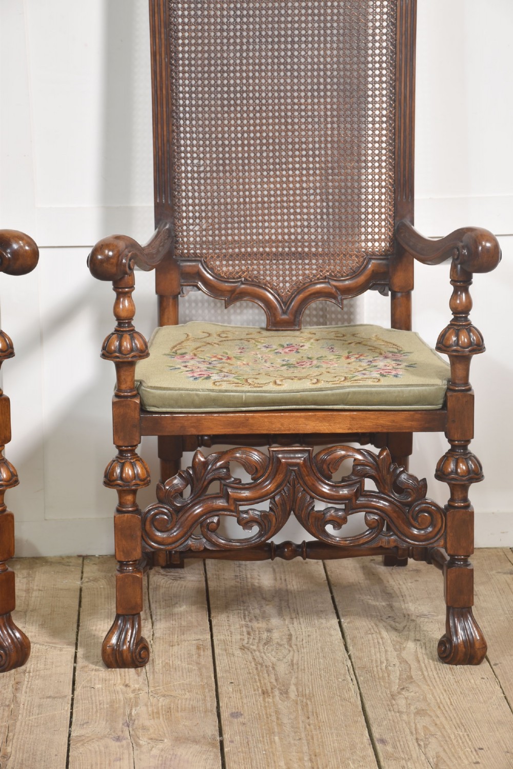 A pair of high-backed carved walnut open armchairs featuring tall cane panels, turned supports, intricate scrolling stretchers, and floral needlepoint cushions. View VII