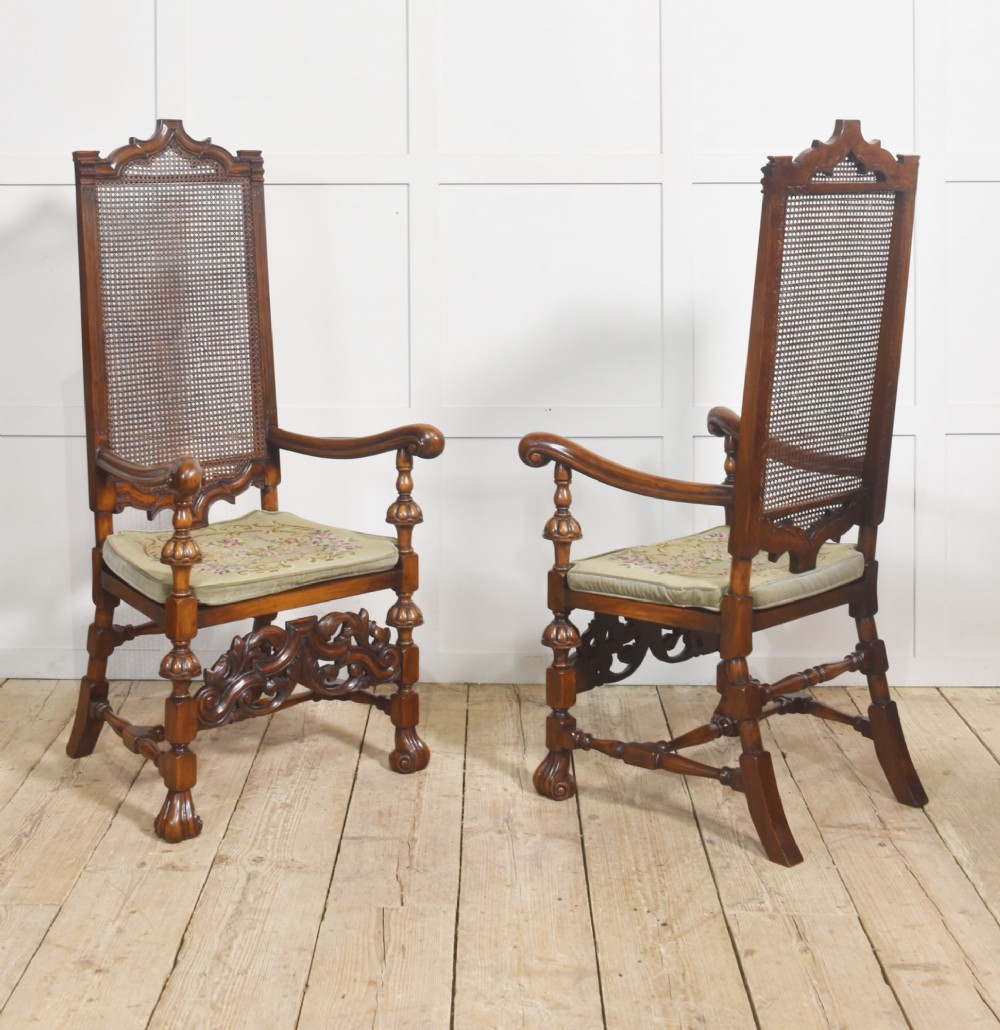 A pair of high-backed carved walnut open armchairs featuring tall cane panels, turned supports, intricate scrolling stretchers, and floral needlepoint cushions. View VIII