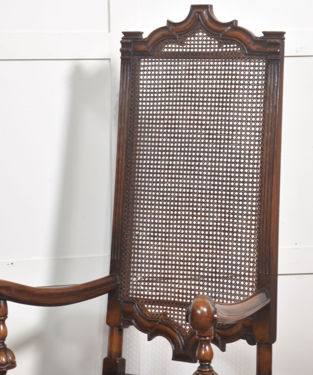 A pair of high-backed carved walnut open armchairs featuring tall cane panels, turned supports, intricate scrolling stretchers, and floral needlepoint cushions. View XI