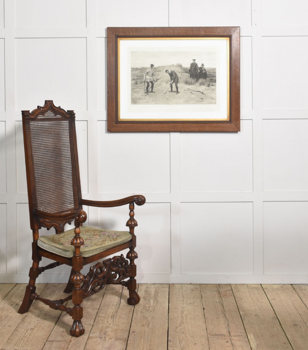 A pair of high-backed carved walnut open armchairs featuring tall cane panels, turned supports, intricate scrolling stretchers, and floral needlepoint cushions. View XII