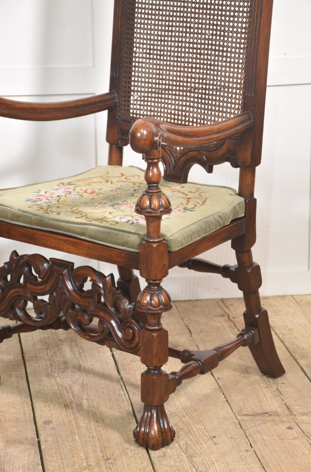 A pair of high-backed carved walnut open armchairs featuring tall cane panels, turned supports, intricate scrolling stretchers, and floral needlepoint cushions. View XIII