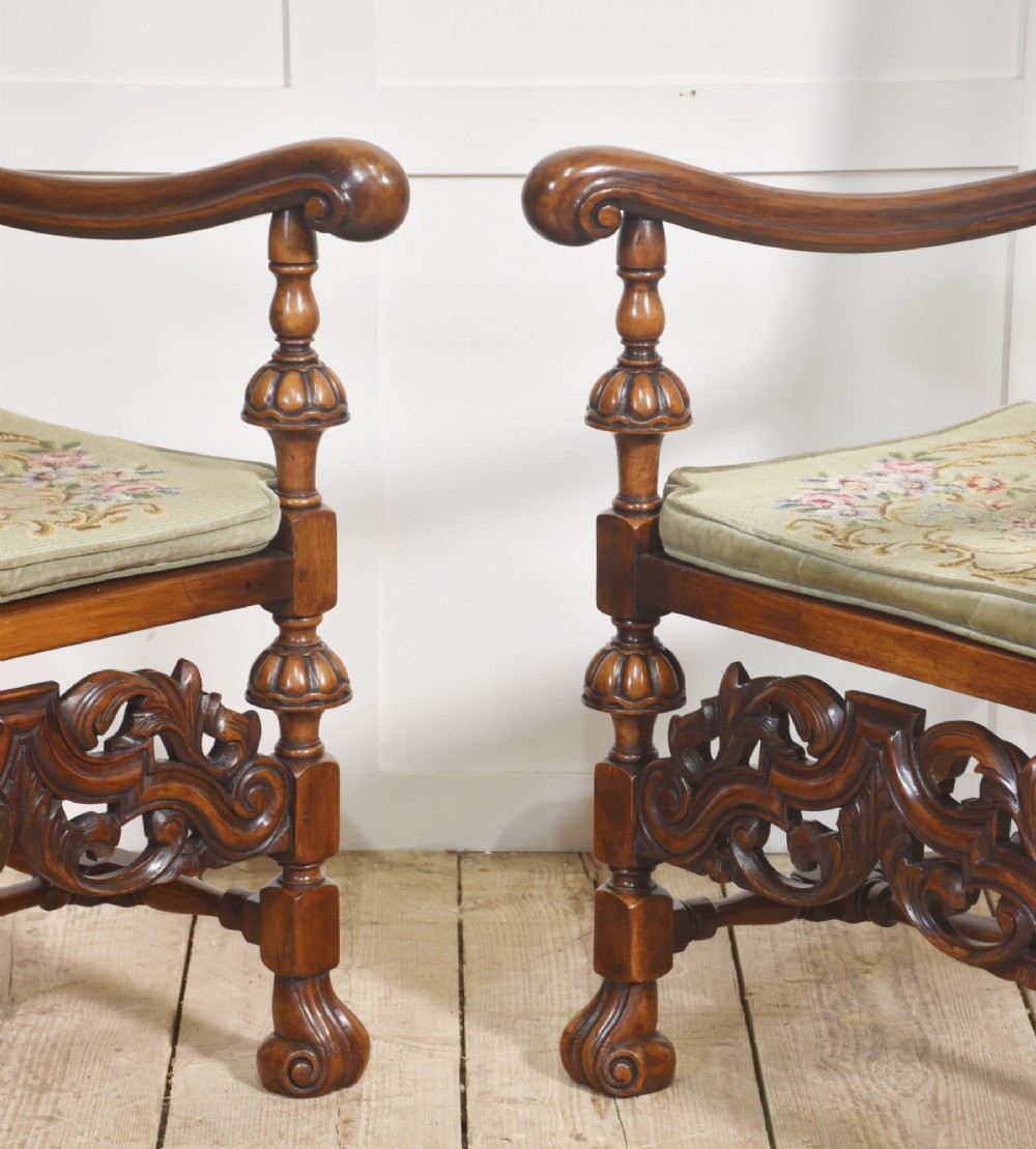 A pair of high-backed carved walnut open armchairs featuring tall cane panels, turned supports, intricate scrolling stretchers, and floral needlepoint cushions. View XIV