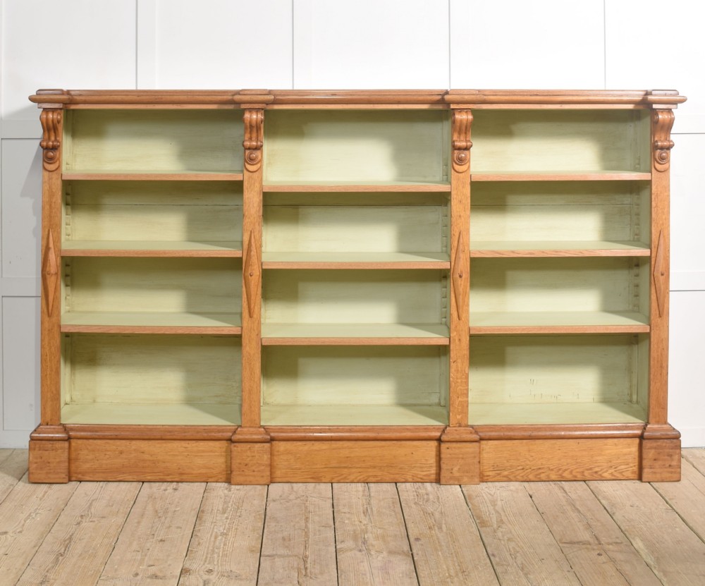 A large 19th-century oak open bookcase featuring three bays, carved decorative corbels, adjustable shelves, and a pale green painted interior. View VI