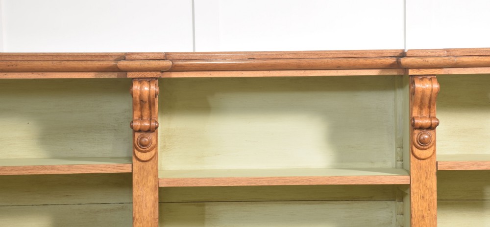 A large 19th-century oak open bookcase featuring three bays, carved decorative corbels, adjustable shelves, and a pale green painted interior. View VII