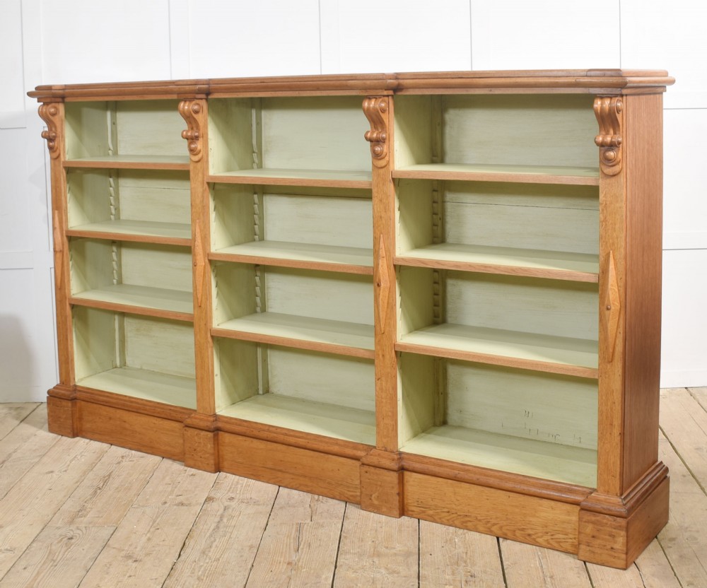 A large 19th-century oak open bookcase featuring three bays, carved decorative corbels, adjustable shelves, and a pale green painted interior. View IX