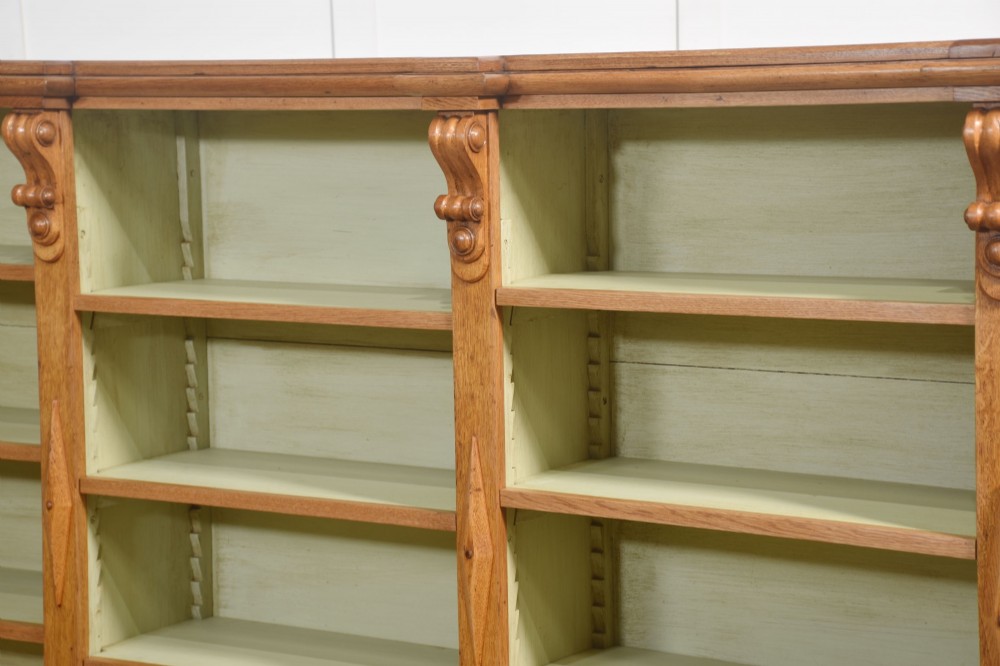 A large 19th-century oak open bookcase featuring three bays, carved decorative corbels, adjustable shelves, and a pale green painted interior. View X