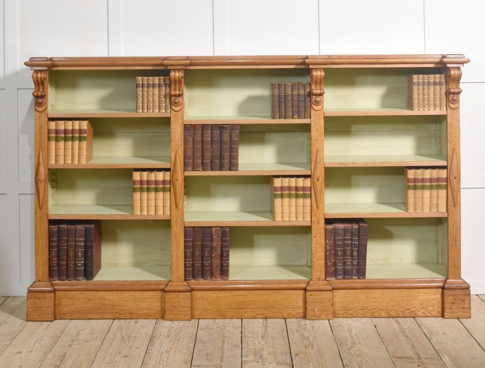 A large 19th-century oak open bookcase featuring three bays, carved decorative corbels, adjustable shelves, and a pale green painted interior.