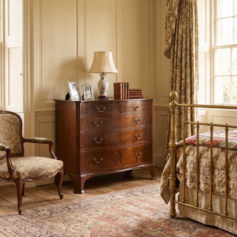 An Edwardian figured mahogany bow front chest of drawers featuring two short over three long drawers with brass swan-neck handles and splayed bracket feet. View II
