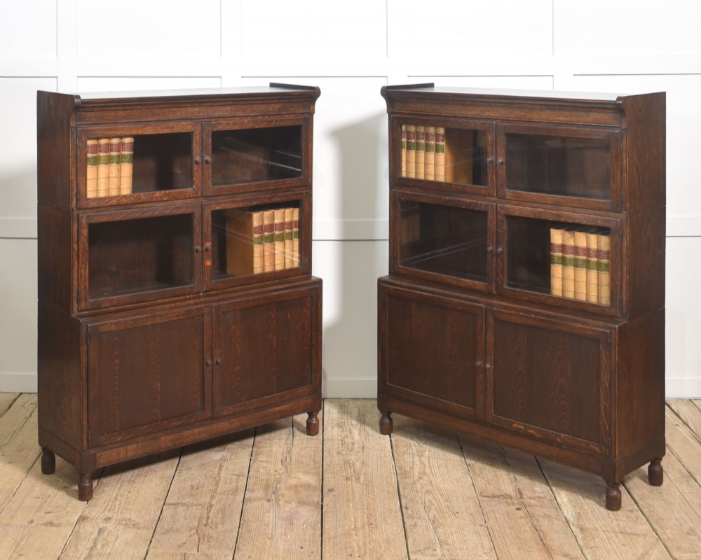 A pair of early twentieth-century dark oak sectional bookcases featuring two glazed upper tiers and a double-door base cupboard on turned feet.
