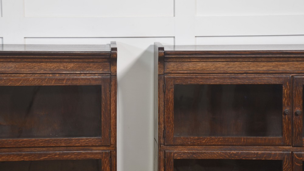A pair of early twentieth-century dark oak sectional bookcases featuring two glazed upper tiers and a double-door base cupboard on turned feet. View VII