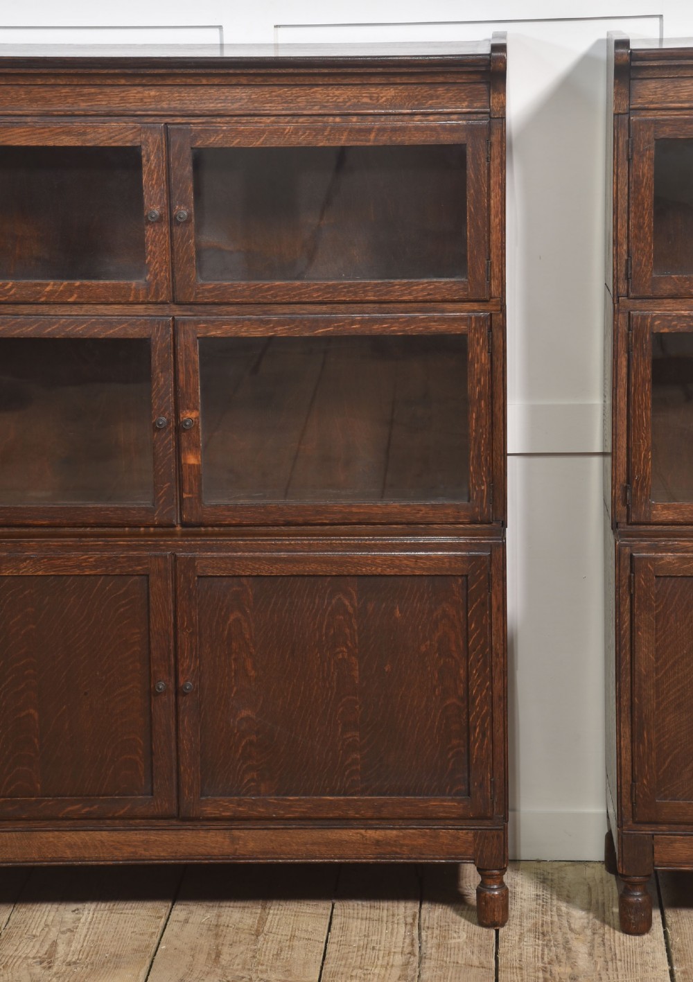 A pair of early twentieth-century dark oak sectional bookcases featuring two glazed upper tiers and a double-door base cupboard on turned feet. View VIII