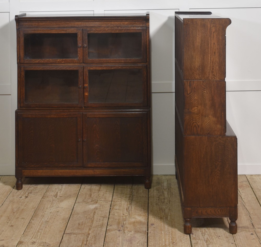 A pair of early twentieth-century dark oak sectional bookcases featuring two glazed upper tiers and a double-door base cupboard on turned feet. View IX