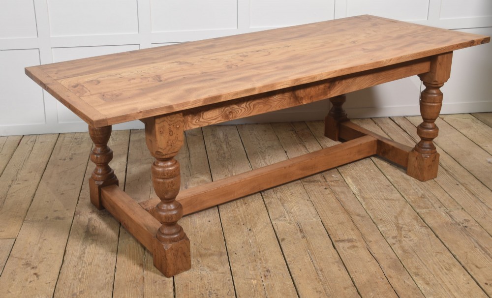 A 19th-century rectangular elm refectory dining table featuring turned wooden legs connected by a central lower stretcher.