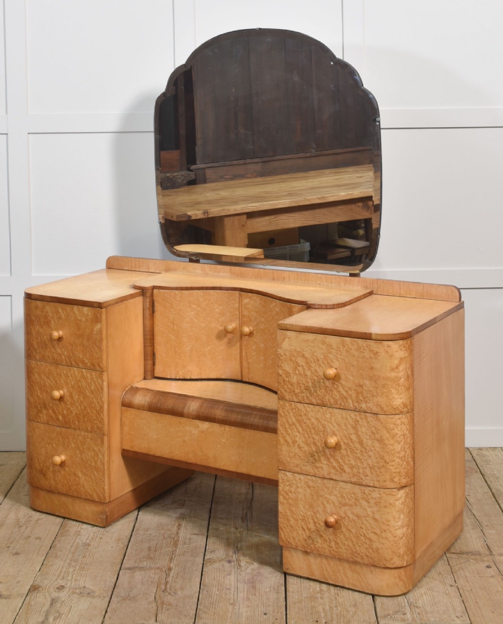 An Art Deco light blonde birds eye maple dressing table featuring curved pedestal drawers, a central cupboard, and a large shaped mirror attached above. View IV