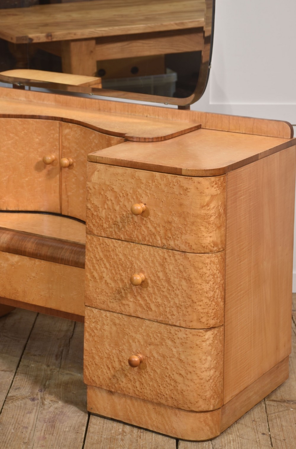 An Art Deco light blonde birds eye maple dressing table featuring curved pedestal drawers, a central cupboard, and a large shaped mirror attached above. View VI