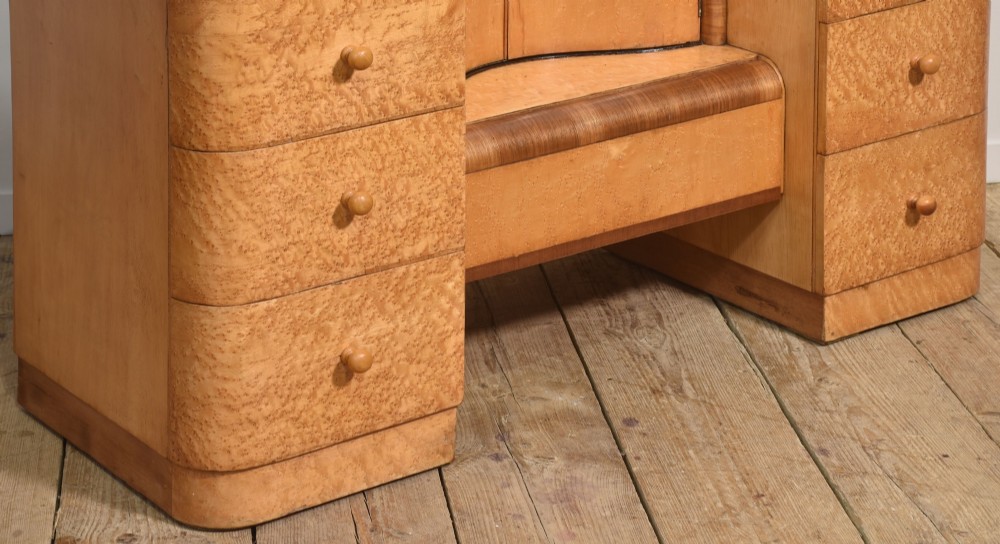 An Art Deco light blonde birds eye maple dressing table featuring curved pedestal drawers, a central cupboard, and a large shaped mirror attached above. View IX
