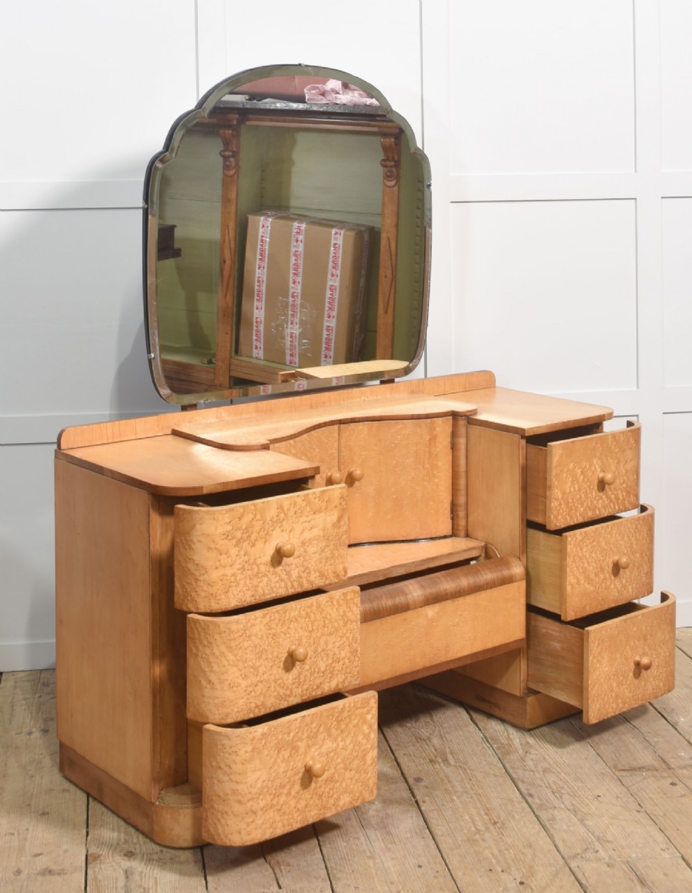 An Art Deco light blonde birds eye maple dressing table featuring curved pedestal drawers, a central cupboard, and a large shaped mirror attached above. View X