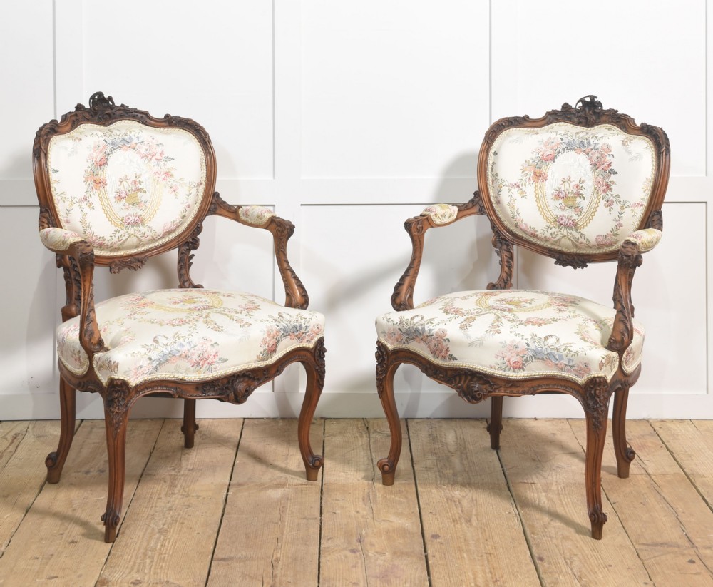 A pair of French carved walnut open armchairs featuring floral tapestry upholstery and cabriole legs.