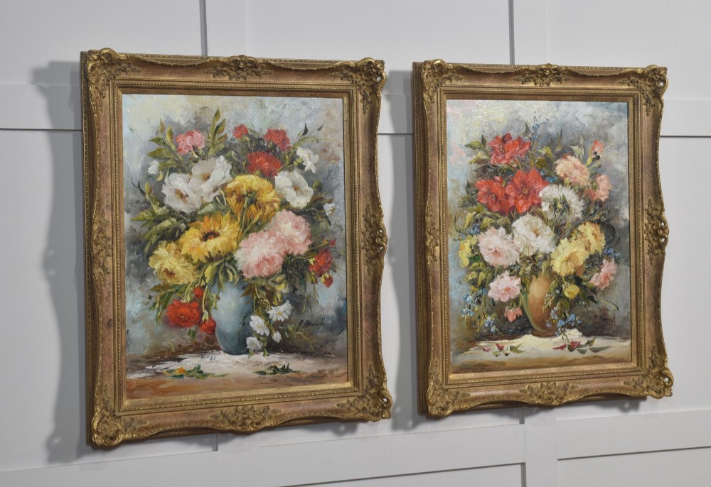 A pair of framed oil paintings depicting colourful arrangements of flowers in ceramic vases set within ornate gilded frames. View V