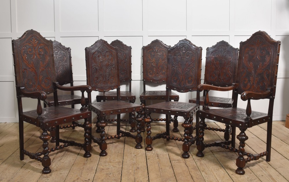 A set of eight dark brown walnut dining chairs featuring embossed floral leather seats and backrests with decorative studding and barley twist legs.
