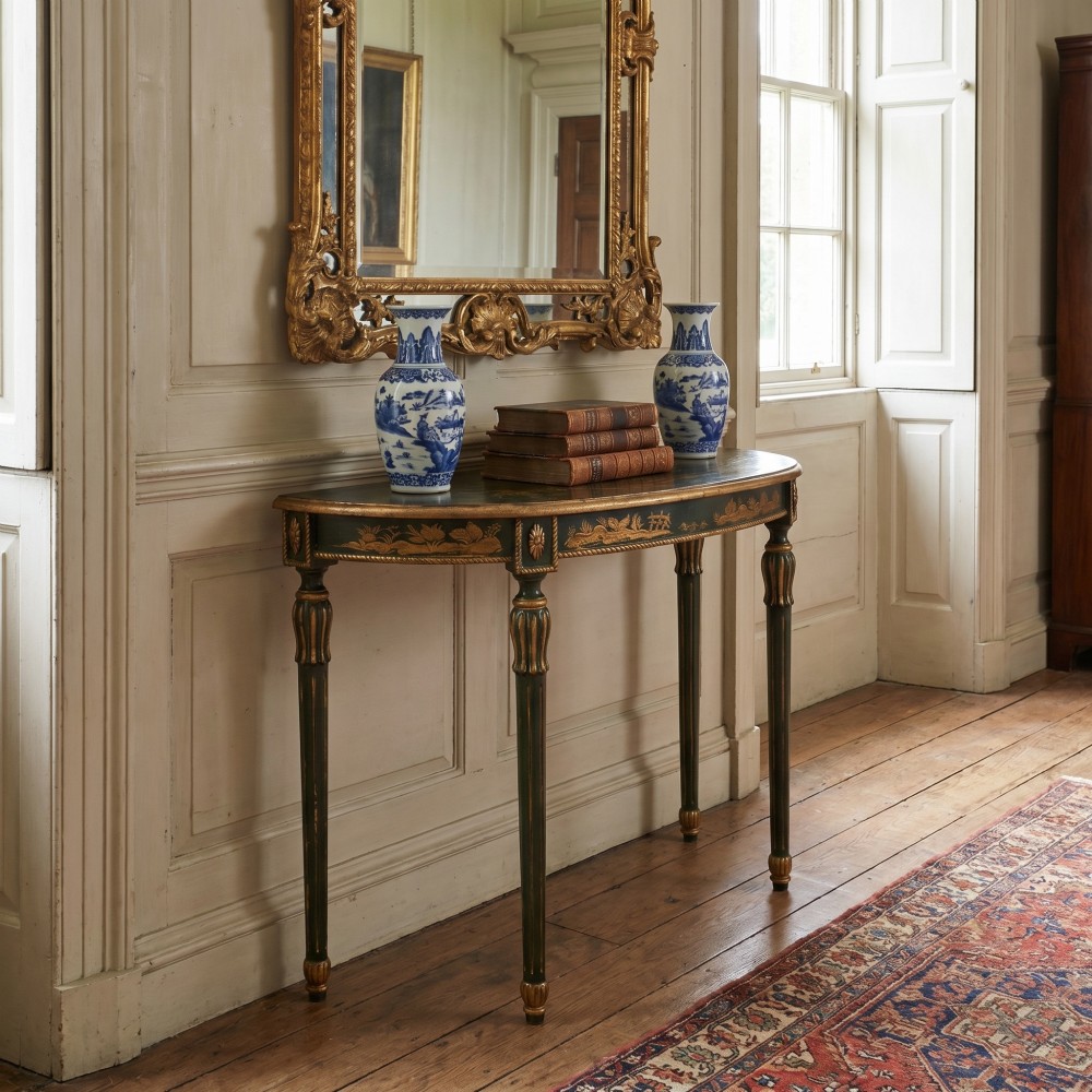 A dark green demi-lune console table with hand-painted gold chinoiserie decoration along the frieze and fluted tapered legs. View II