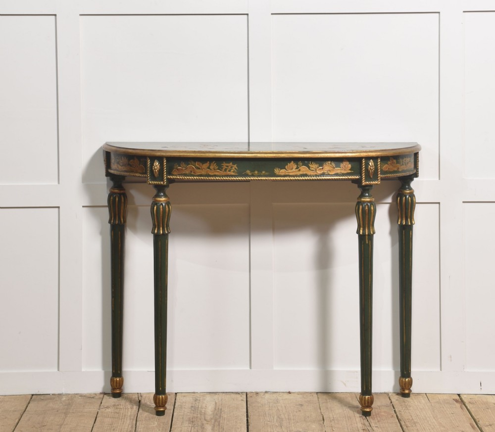 A dark green demi-lune console table with hand-painted gold chinoiserie decoration along the frieze and fluted tapered legs.