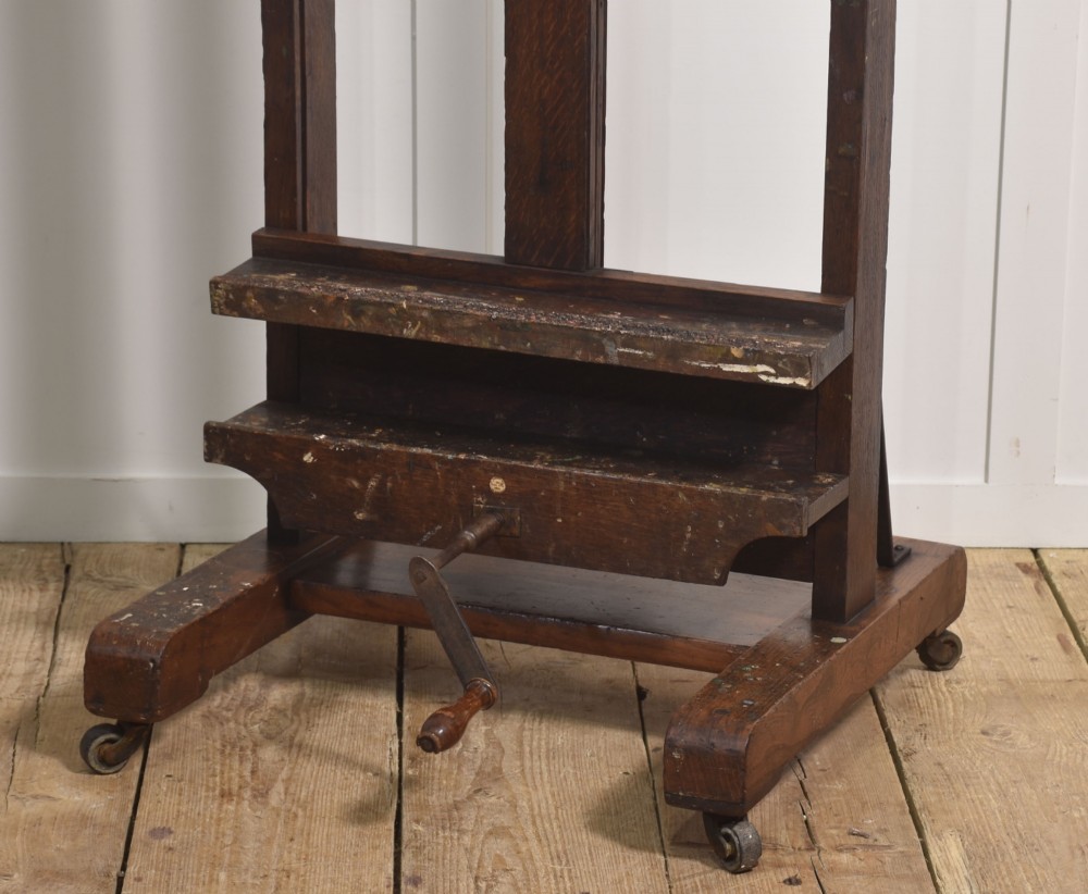 A dark oak adjustable artist studio easel featuring a hand-crank winding mechanism and a castored base. View III