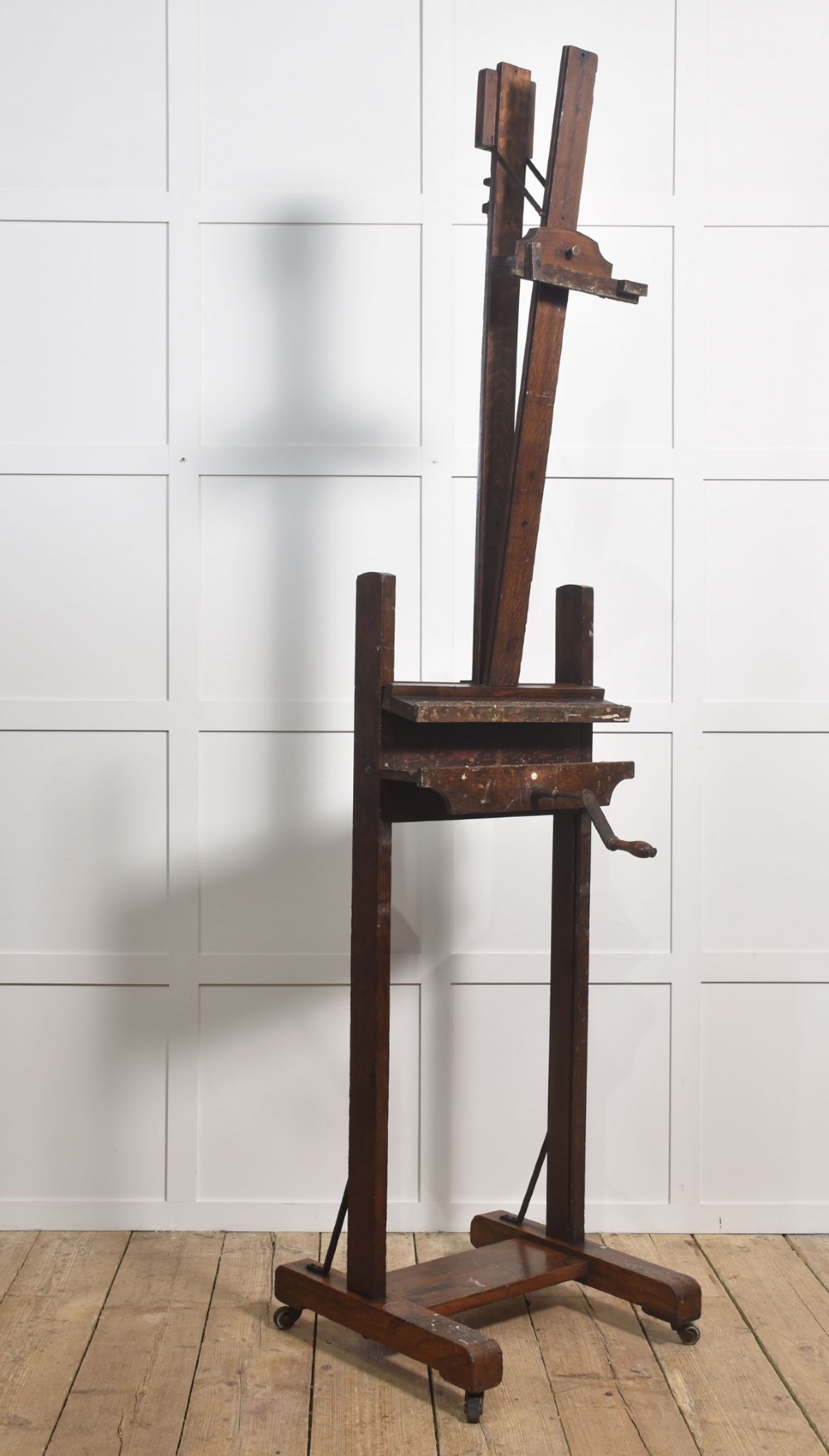 A dark oak adjustable artist studio easel featuring a hand-crank winding mechanism and a castored base. View IX