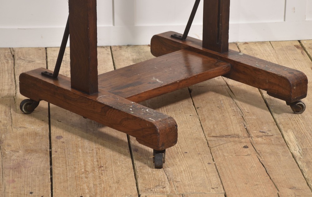 A dark oak adjustable artist studio easel featuring a hand-crank winding mechanism and a castored base. View X