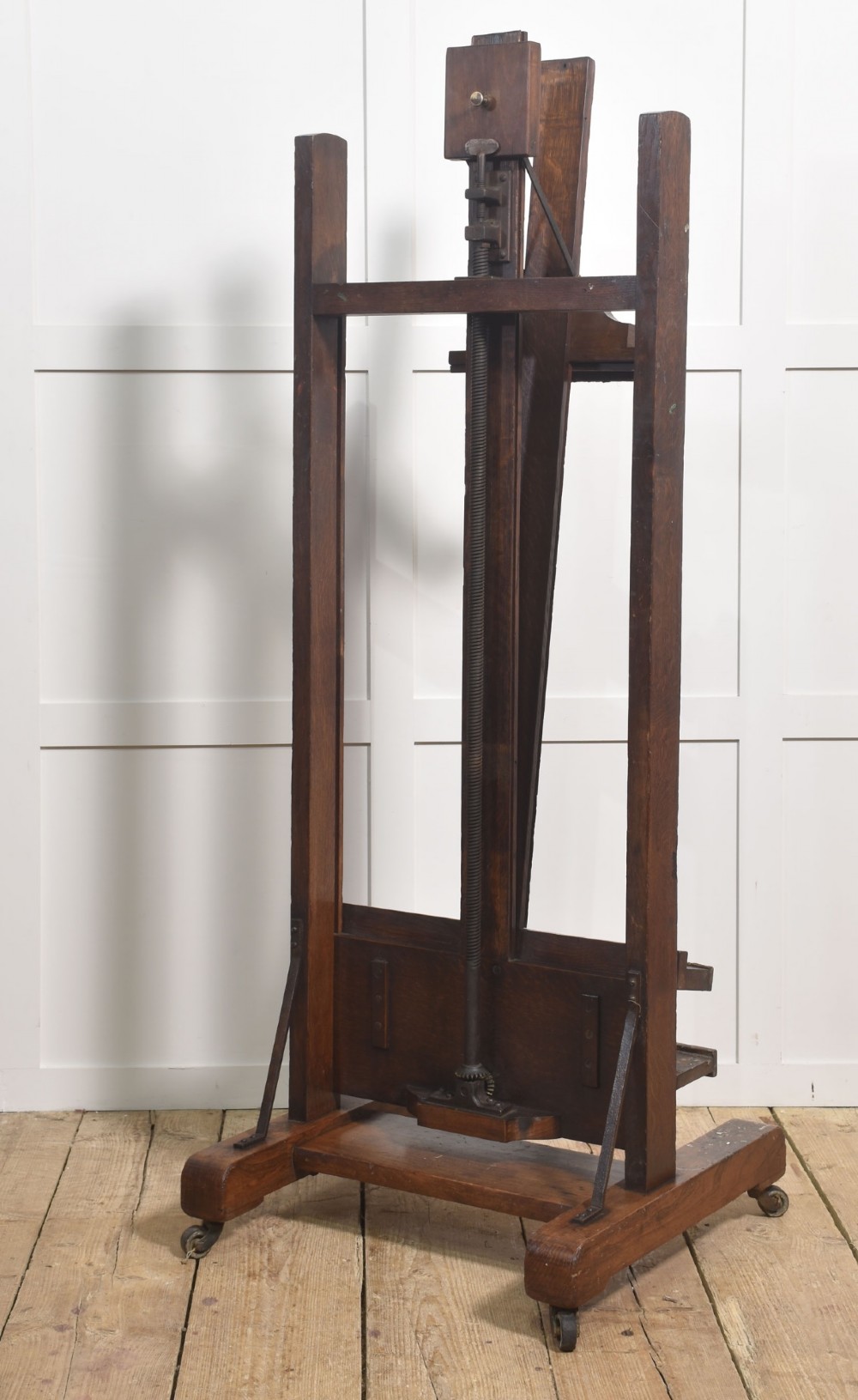 A dark oak adjustable artist studio easel featuring a hand-crank winding mechanism and a castored base. View XII