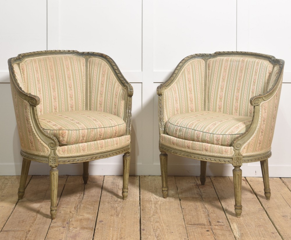 A pair of grey-painted French tub armchairs upholstered in a striped floral pastel fabric with fluted legs.