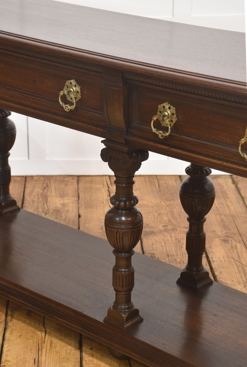 A dark oak Jacobean style dresser base featuring three drawers with decorative brass handles, turned baluster legs, and a full-length lower pot board shelf. View VIII