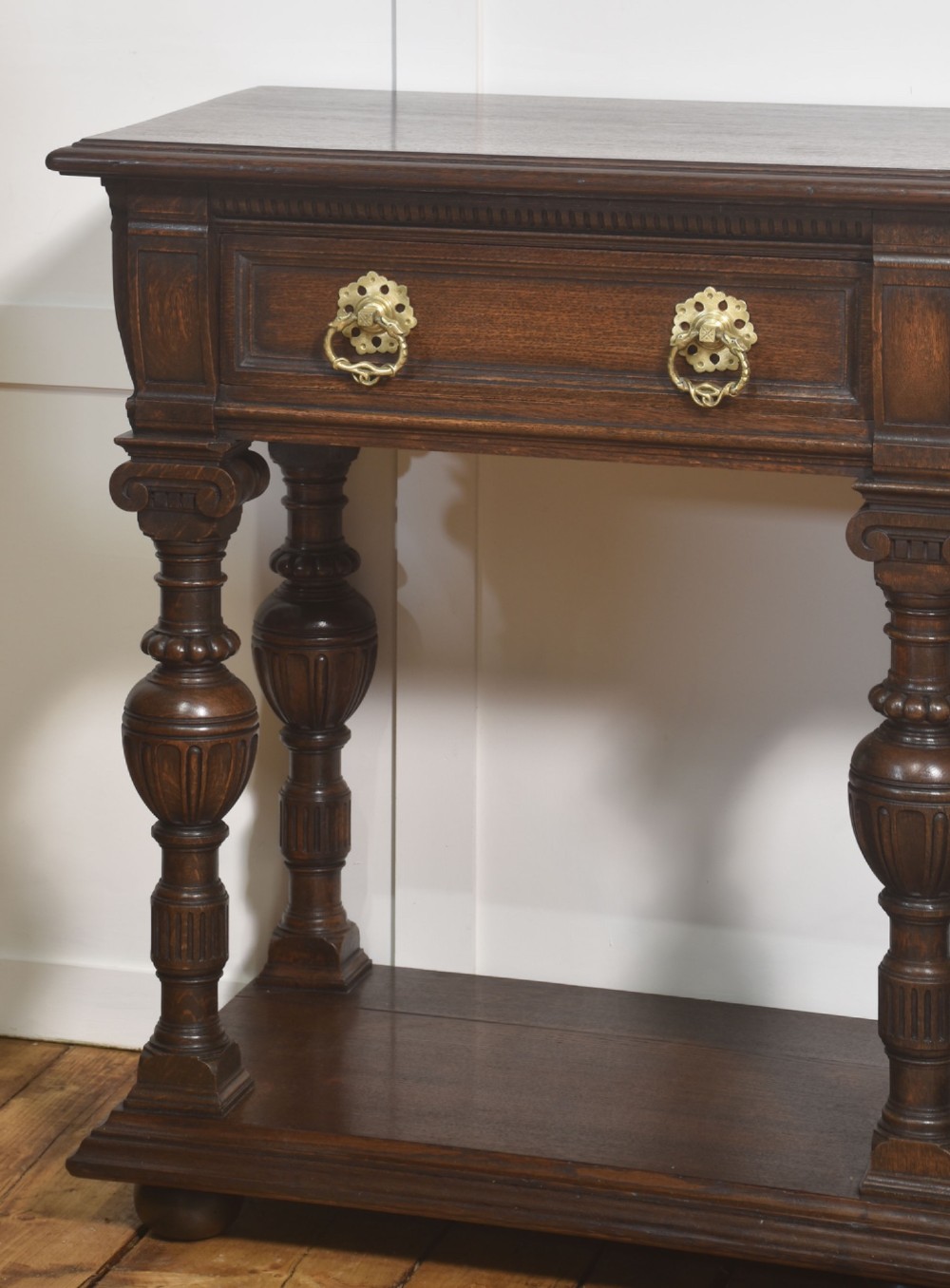 A dark oak Jacobean style dresser base featuring three drawers with decorative brass handles, turned baluster legs, and a full-length lower pot board shelf. View XIII