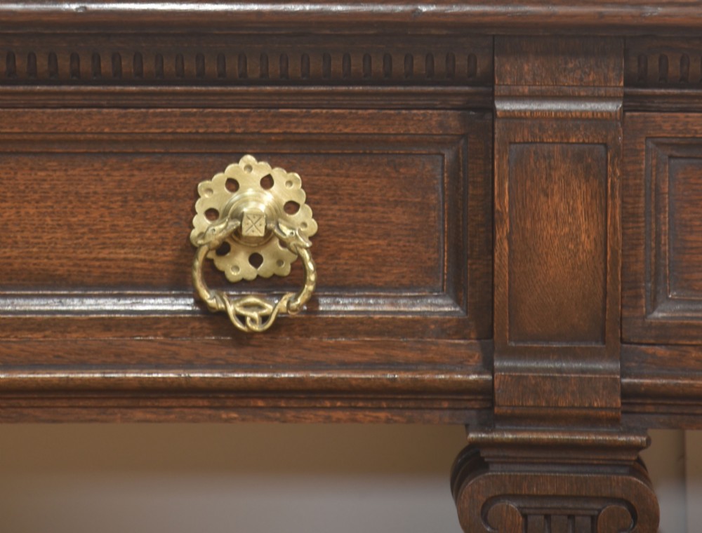 A dark oak Jacobean style dresser base featuring three drawers with decorative brass handles, turned baluster legs, and a full-length lower pot board shelf. View XV