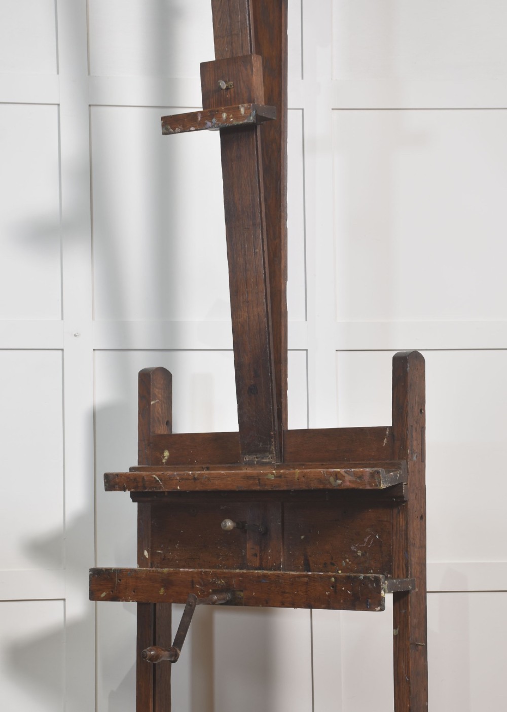 A late nineteenth-century dark oak artist studio easel featuring an adjustable central shaft, crank handle, and cast iron castors on an H-frame base. View IV