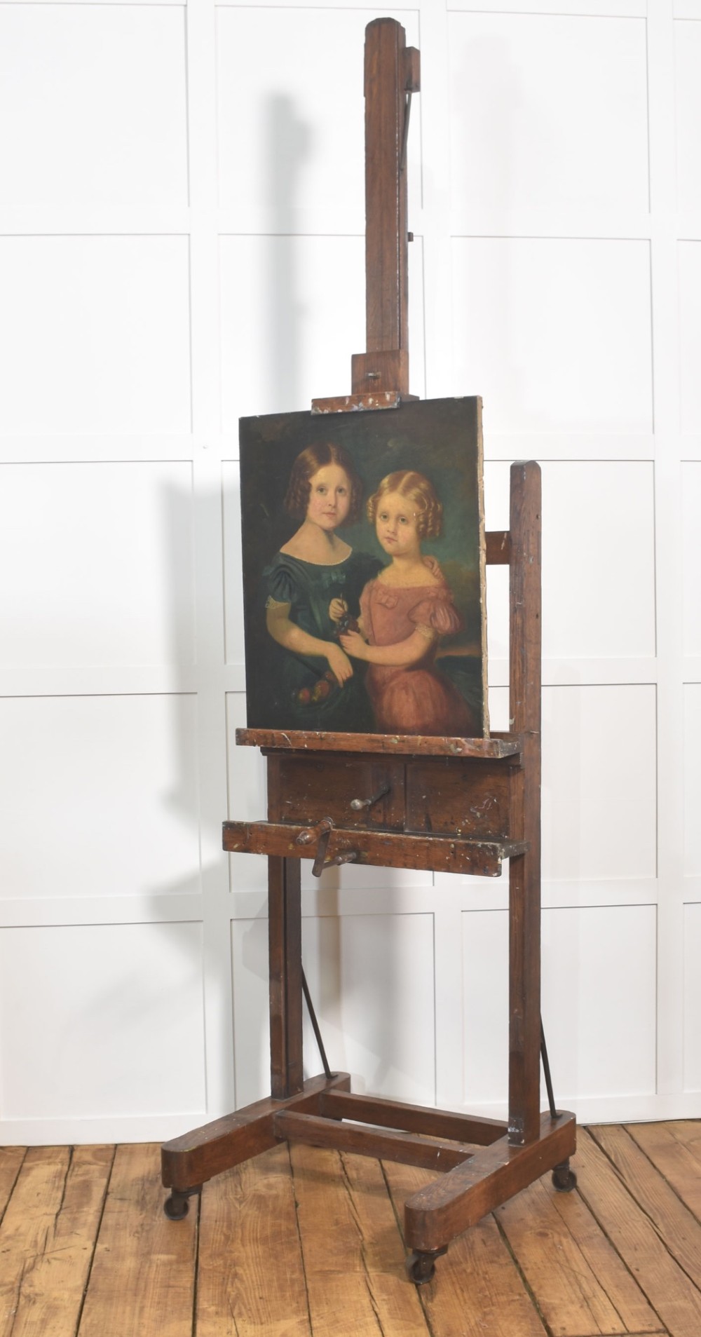 A late nineteenth-century dark oak artist studio easel featuring an adjustable central shaft, crank handle, and cast iron castors on an H-frame base. View VI