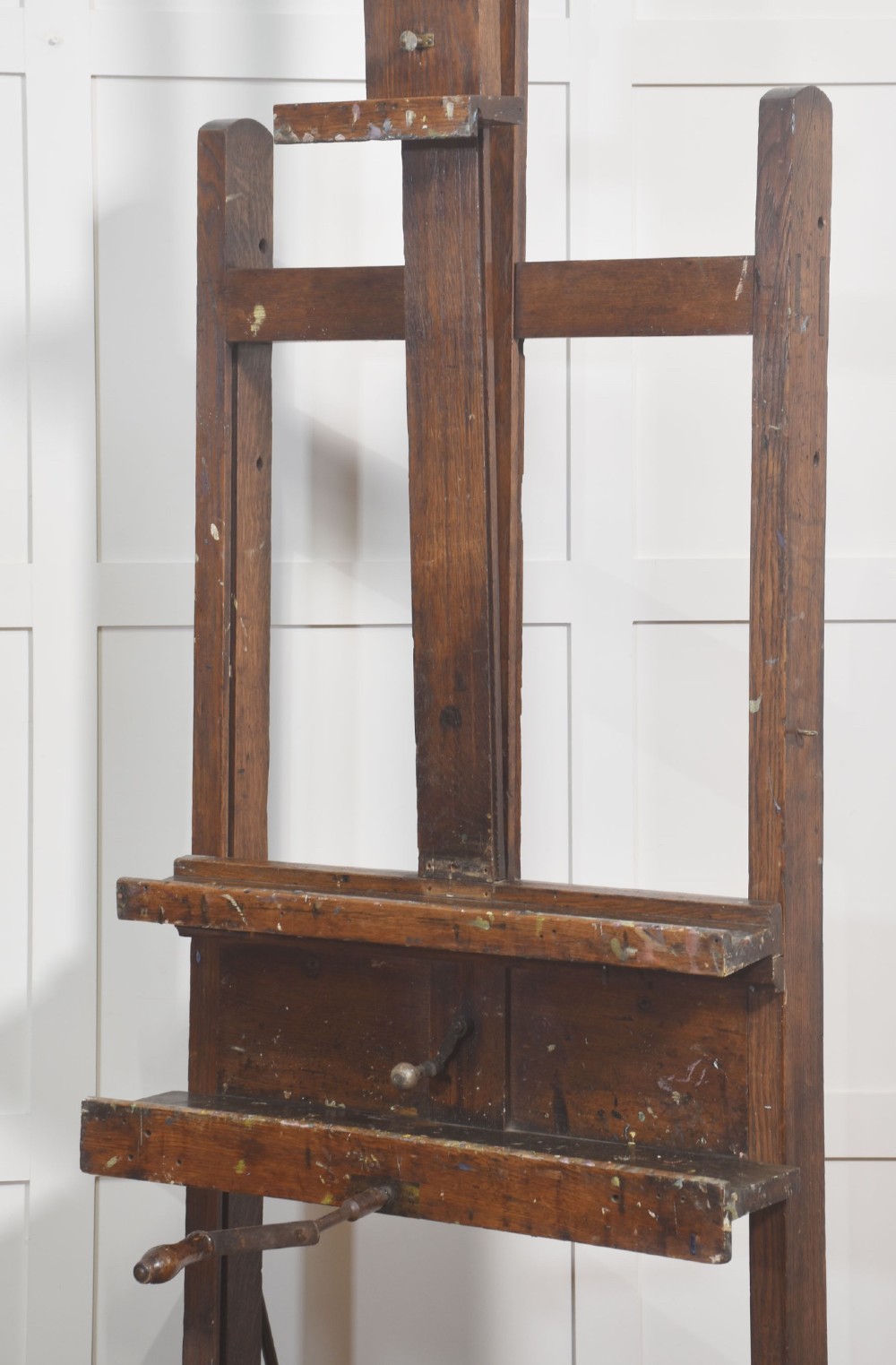 A late nineteenth-century dark oak artist studio easel featuring an adjustable central shaft, crank handle, and cast iron castors on an H-frame base. View IX