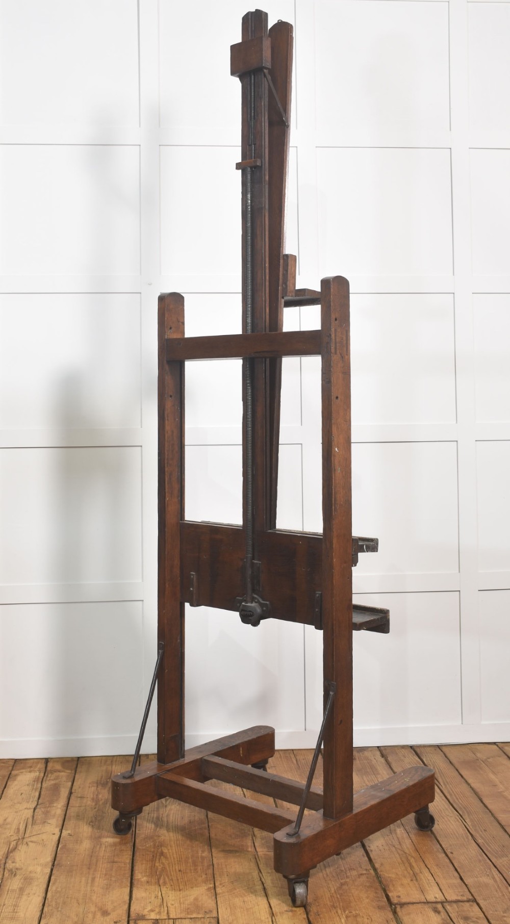 A late nineteenth-century dark oak artist studio easel featuring an adjustable central shaft, crank handle, and cast iron castors on an H-frame base. View XII