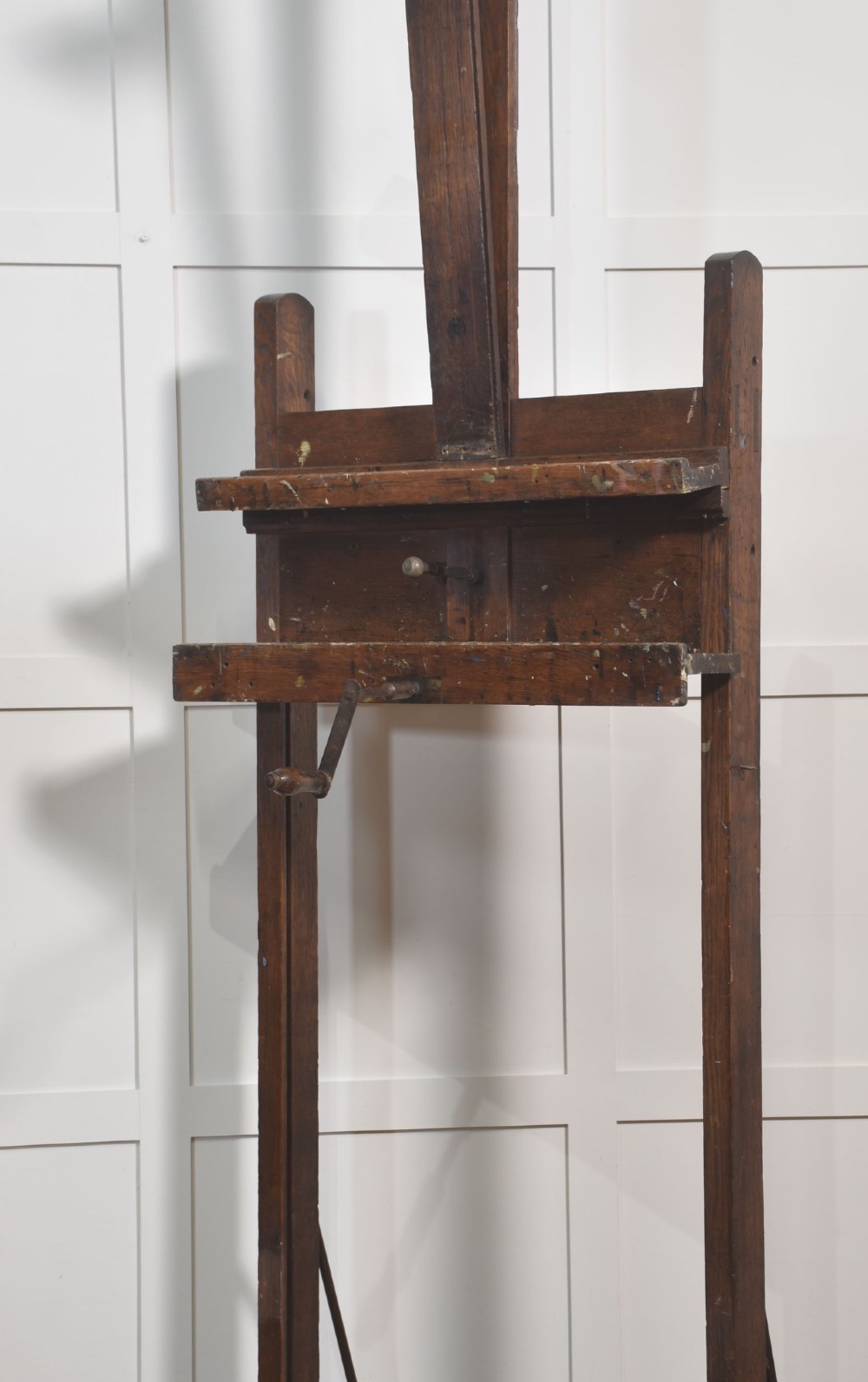 A late nineteenth-century dark oak artist studio easel featuring an adjustable central shaft, crank handle, and cast iron castors on an H-frame base. View XV