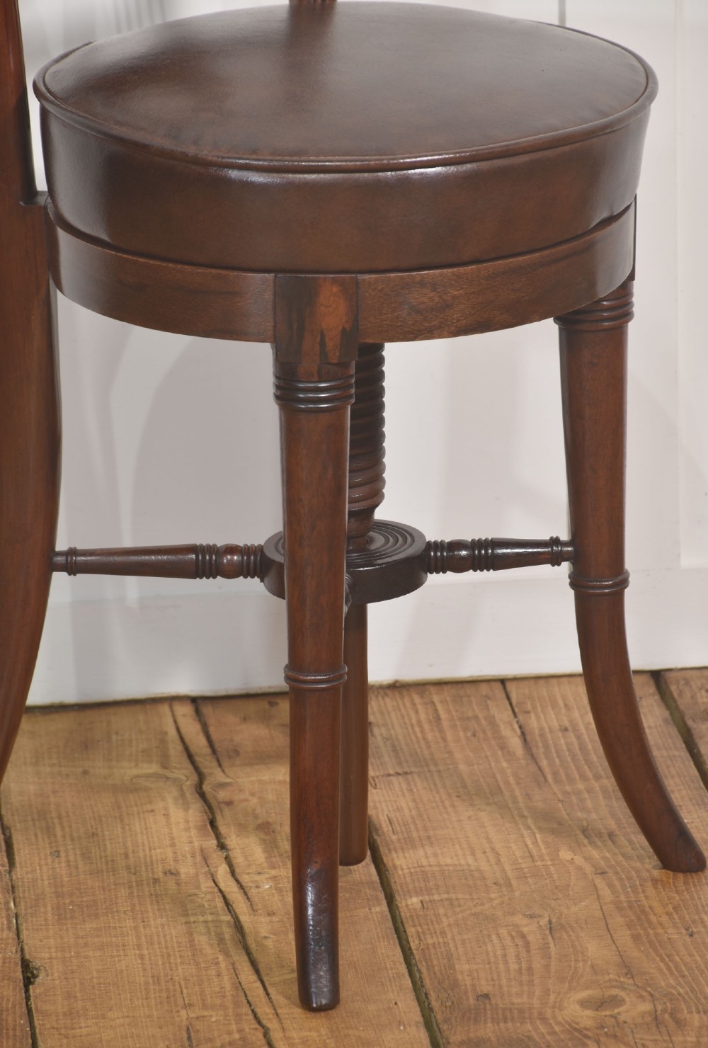 A 19th-century mahogany adjustable chair featuring a carved lyre backrest with brass details, a circular dark leather padded seat, and turned legs. View III