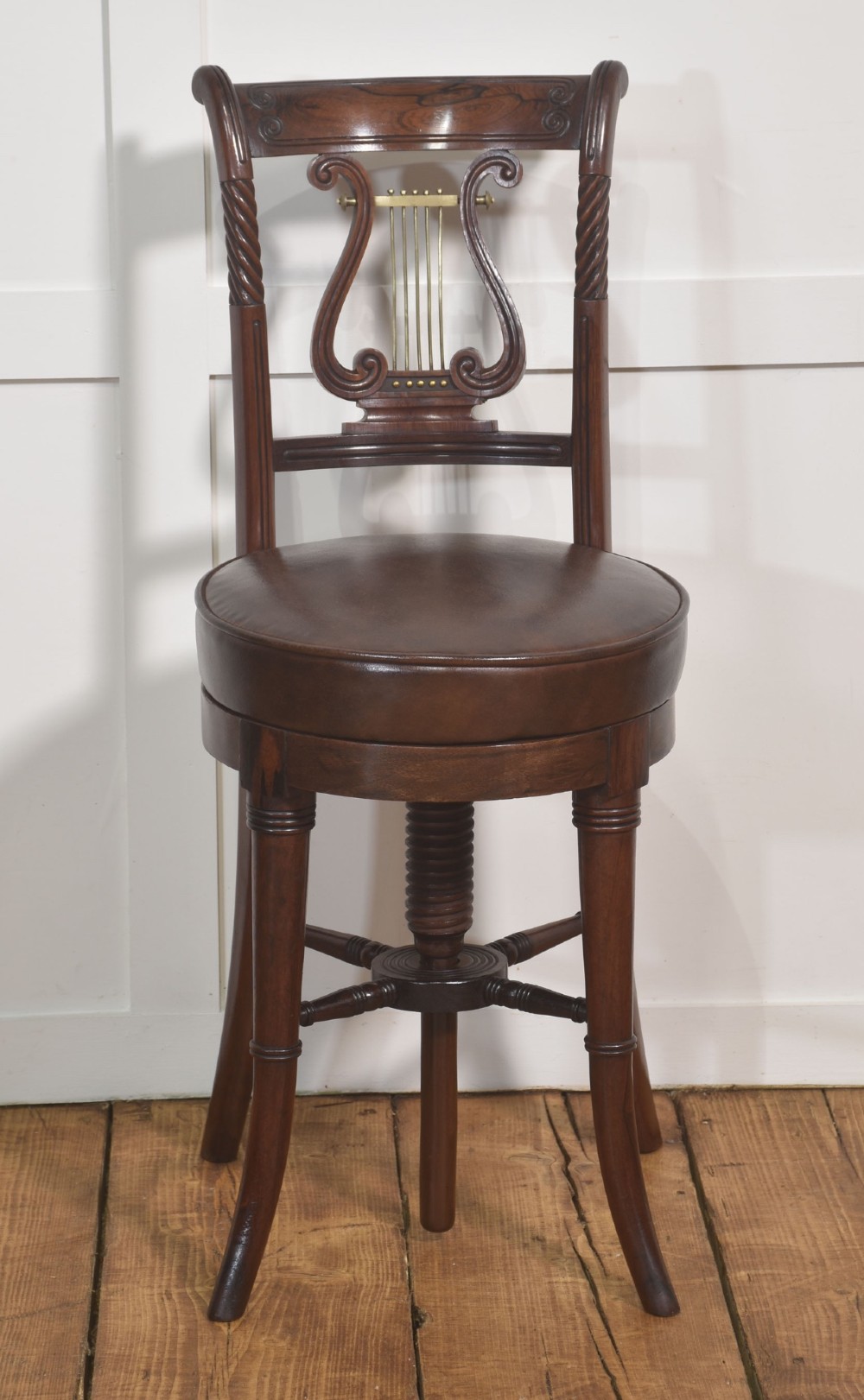A 19th-century mahogany adjustable chair featuring a carved lyre backrest with brass details, a circular dark leather padded seat, and turned legs. View V