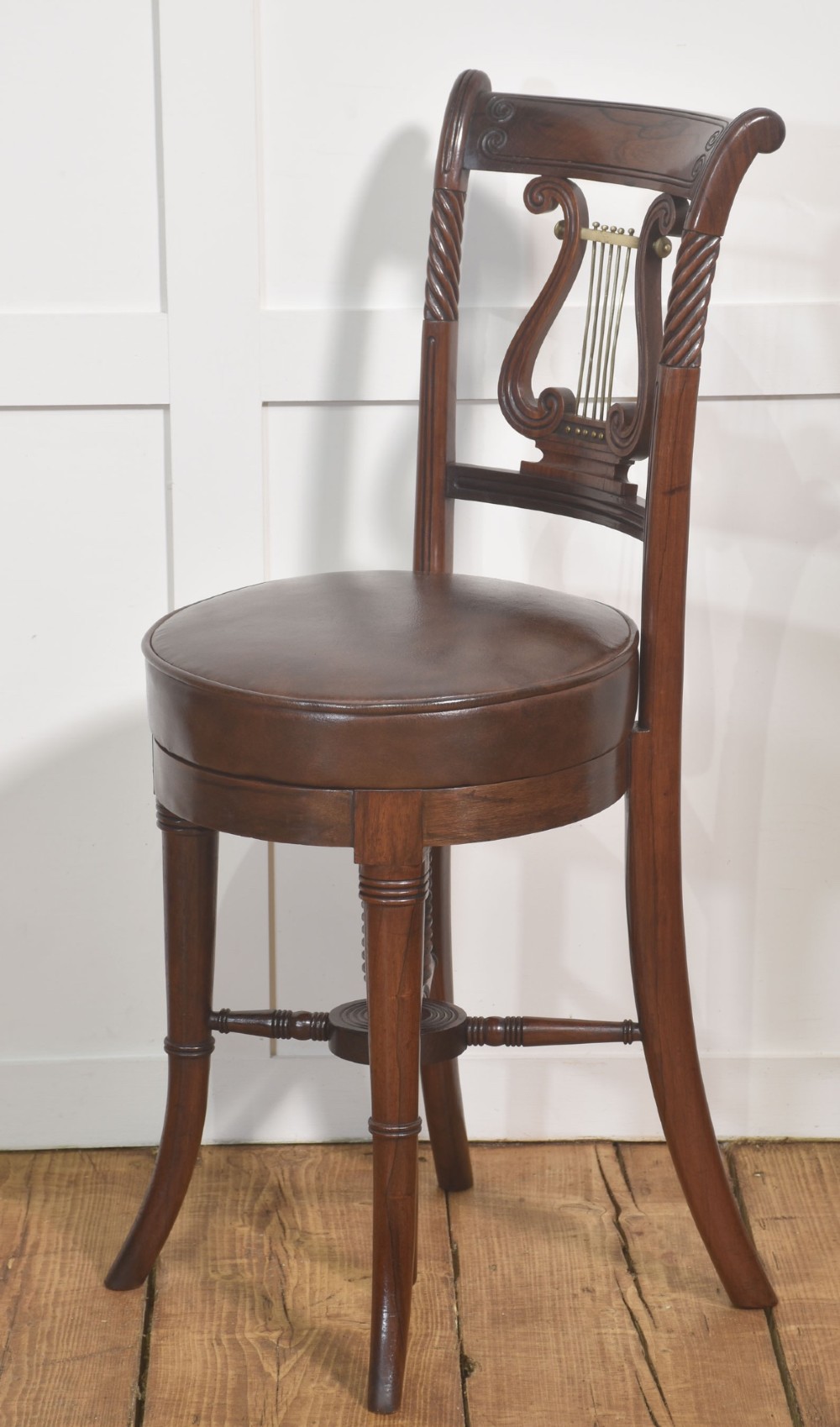 A 19th-century mahogany adjustable chair featuring a carved lyre backrest with brass details, a circular dark leather padded seat, and turned legs. View VI