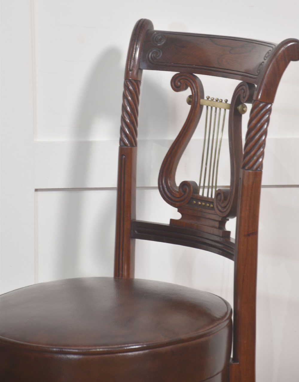 A 19th-century mahogany adjustable chair featuring a carved lyre backrest with brass details, a circular dark leather padded seat, and turned legs. View VII